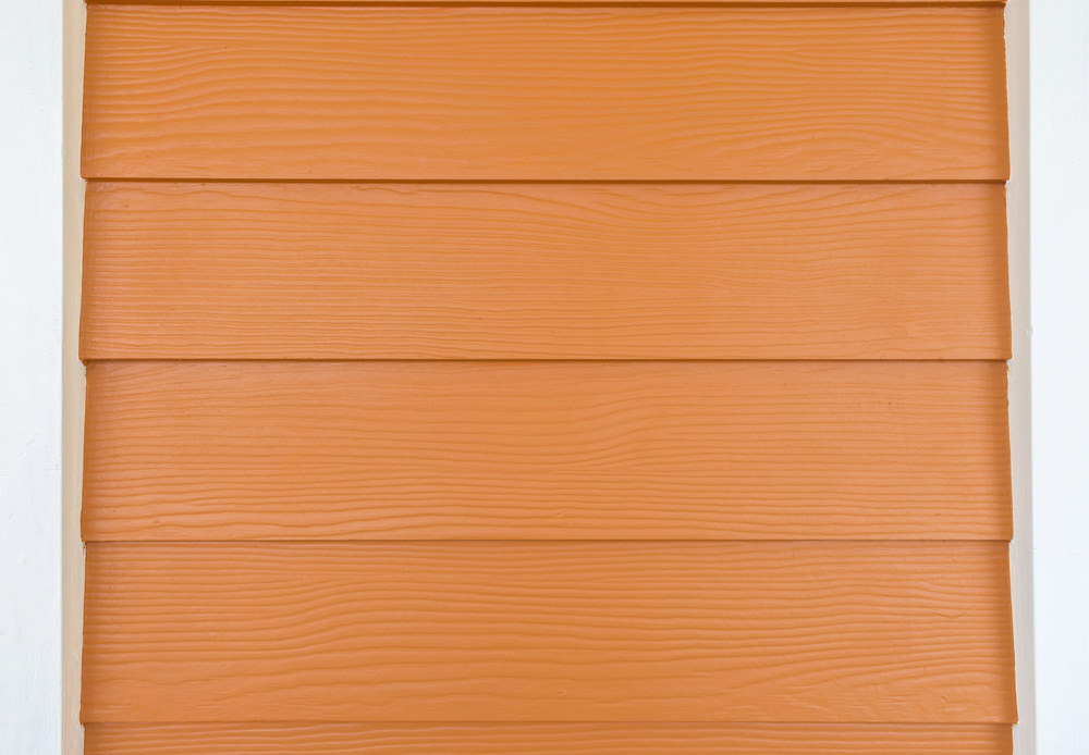 Close-up of orange horizontal wooden siding panels with a textured grain pattern, bordered by white vertical trim on each side.