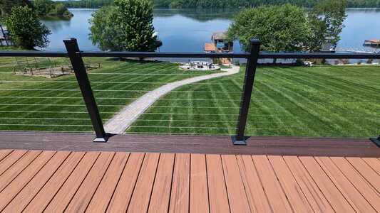 View from a wooden deck overlooking a neatly mowed lawn, a stone path, trees, and a lake with docks in the background.